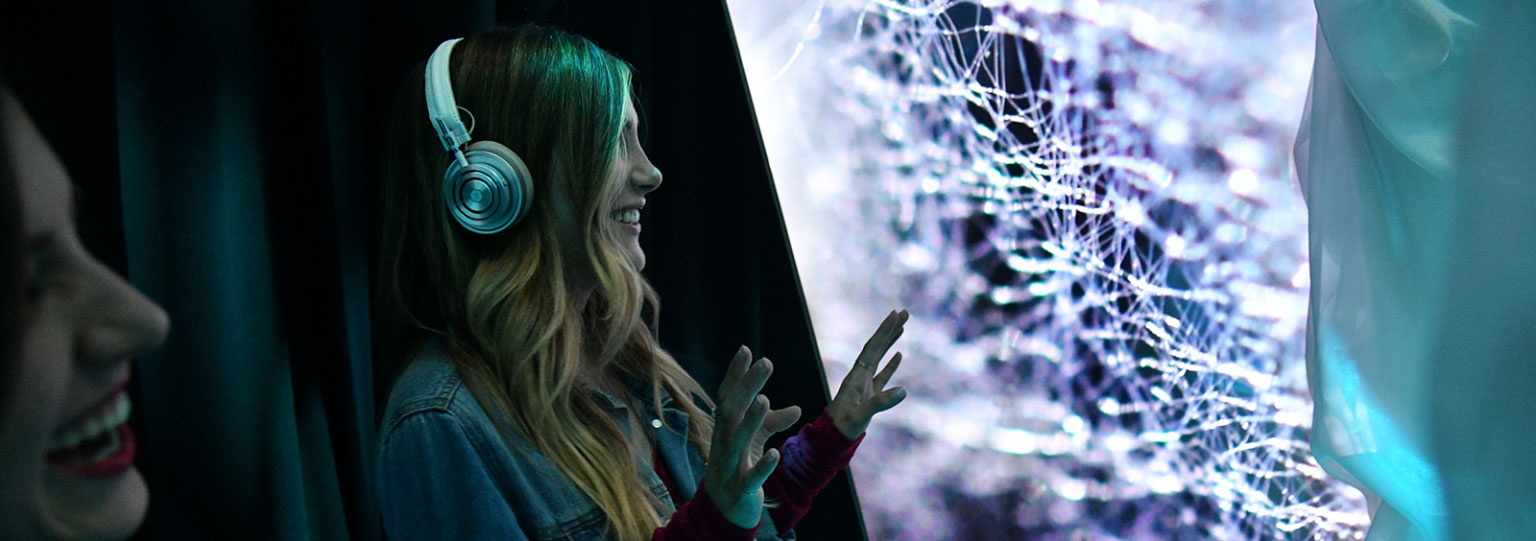 Girl standing in front of installation with headphones on.